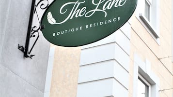 A green sign with "The Lane Boutique Residence" written on it, attached to a building with a wrought iron fence and a "Park Lane" sign below.