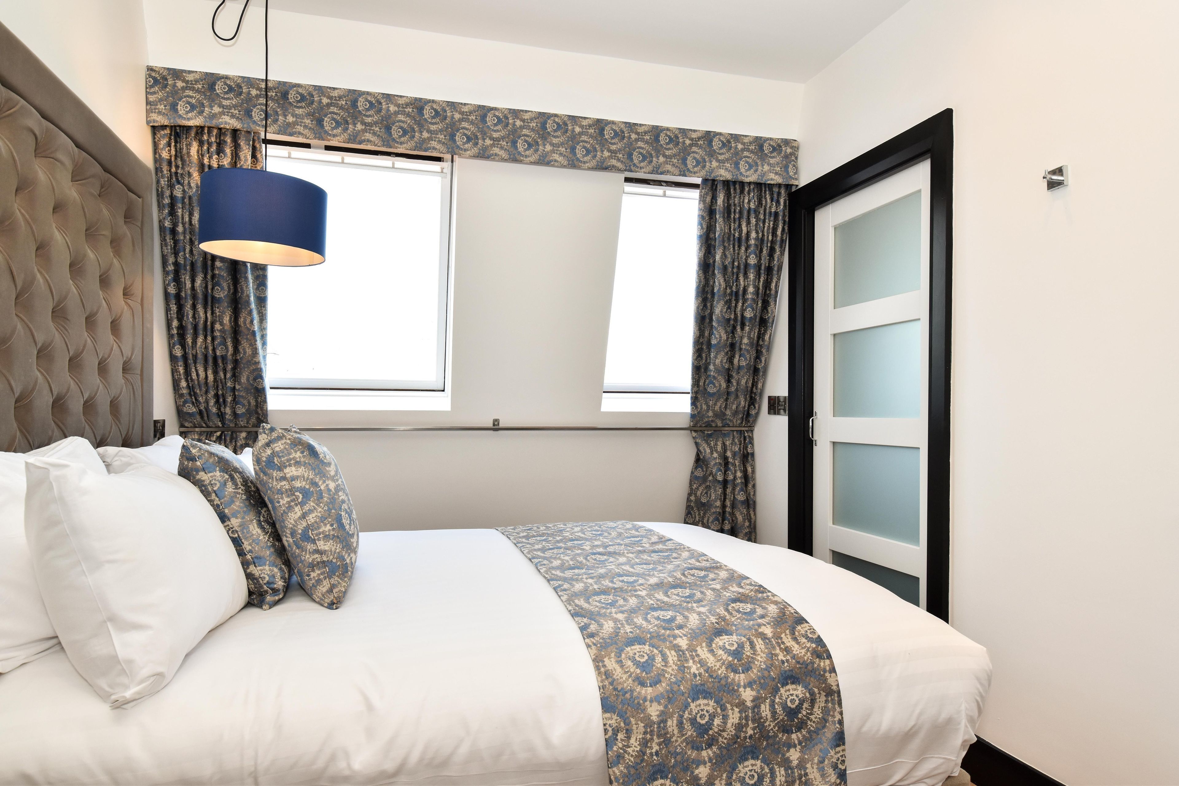 A bedroom with a bed, patterned curtains, a blue hanging lamp, and a door with frosted glass panels.