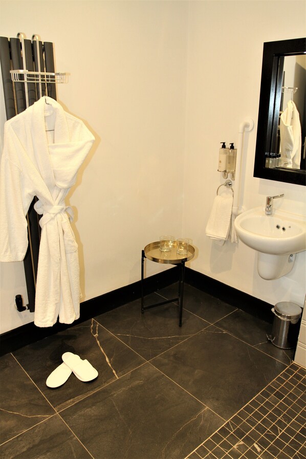 A bathroom with a white bathtub, a sink, and a mirror. There is a pair of slippers on the floor. - The Lane - Boutique Residence (Galway)