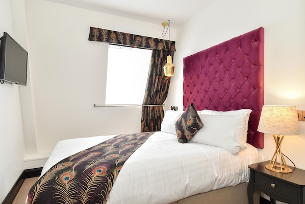 A bedroom with a large bed, a peacock-themed bedspread, a red upholstered headboard, a bedside lamp, and a television on the wall. - The Lane - Boutique Residence (Galway)