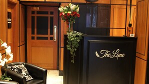 A reception area with a wooden interior, a reception desk labeled "The Lane Boutique Residence," a clock, and a floral arrangement. - The Lane - Boutique Residence (Galway)