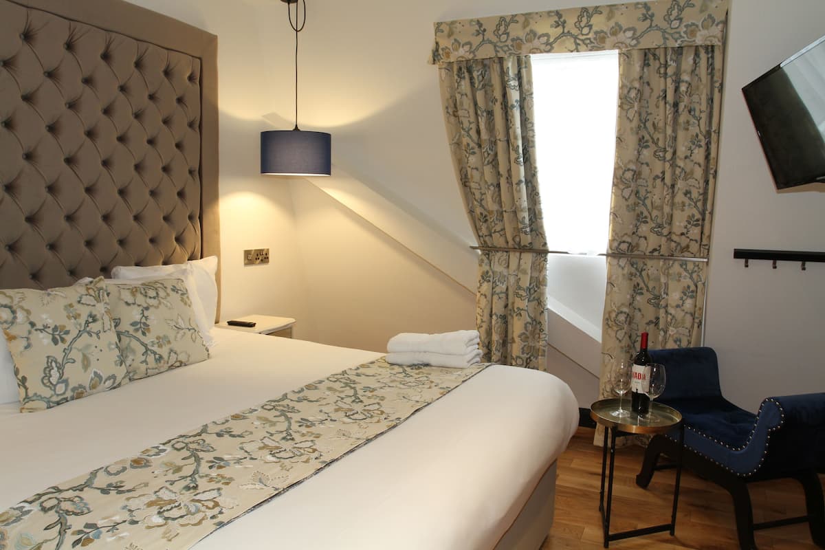 A hotel room with a large bed, a small table with a bottle of wine, a chair, and a TV mounted on the wall.