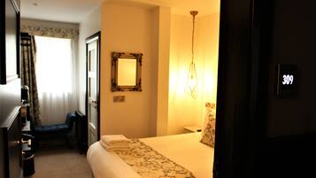 A hotel room with a bed, a nightstand, a mirror, and a wall-mounted light fixture.