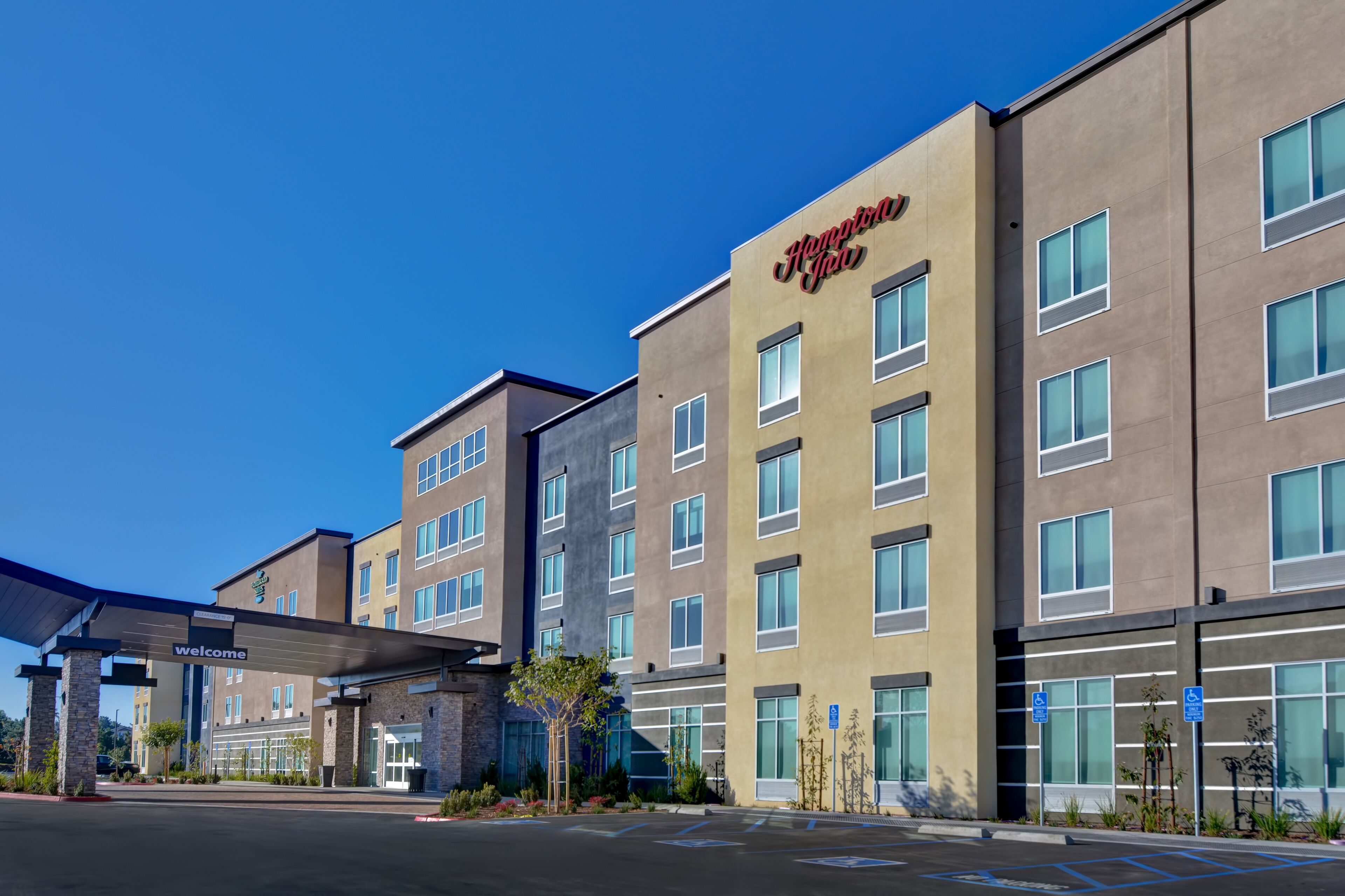 A modern hotel with a 'Welcome' sign, multiple floors, and a parking lot.