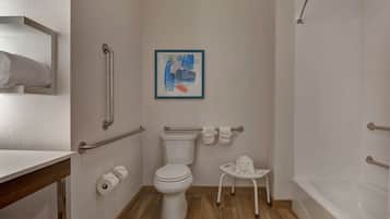 A bathroom with a toilet, handrails, a framed abstract painting, a small table with a tissue box, and a bathtub.