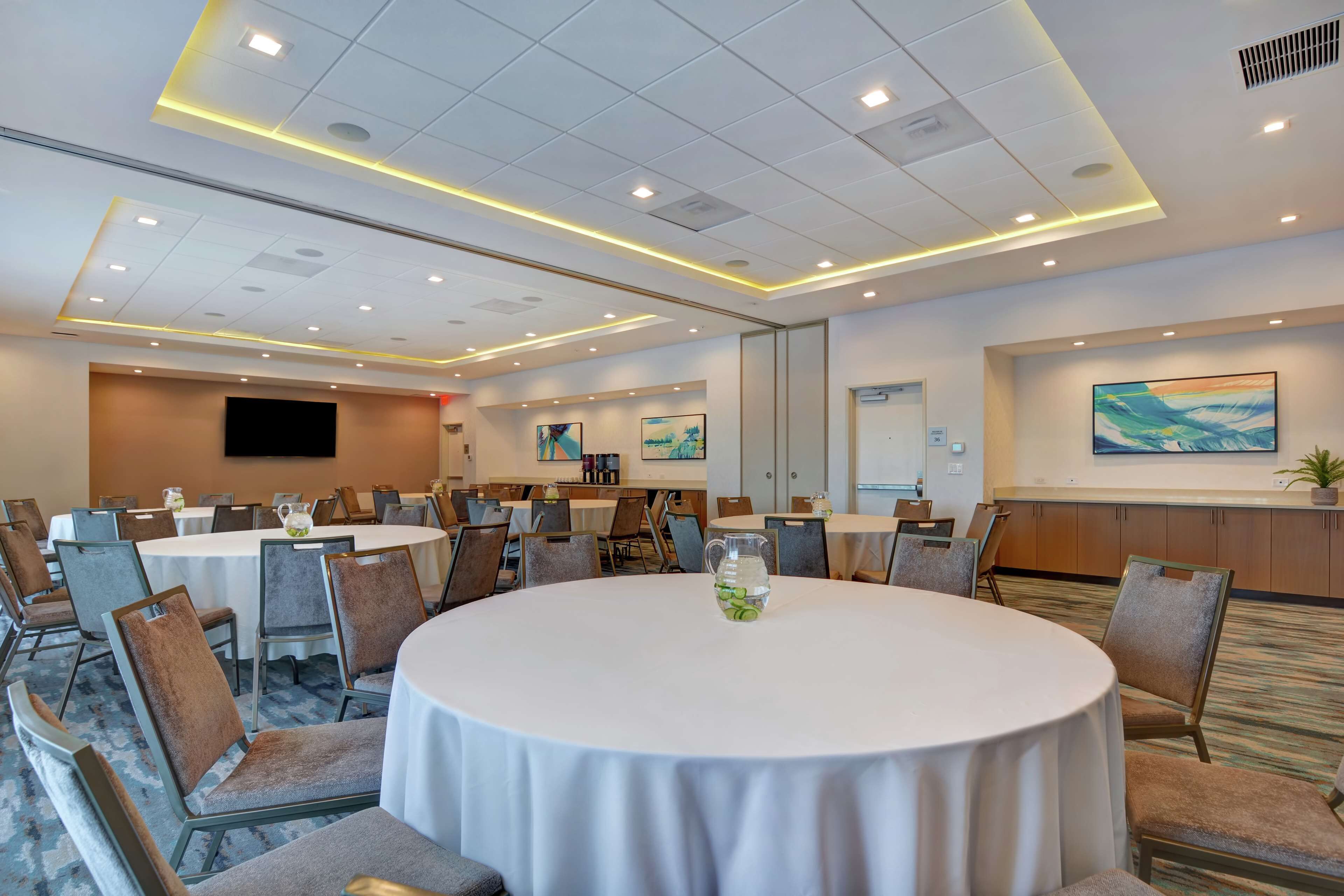 A conference room with round tables, chairs, and a large screen.