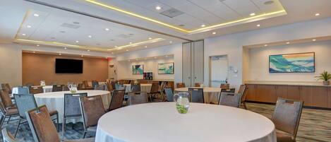 A conference room with round tables, chairs, and a large screen.