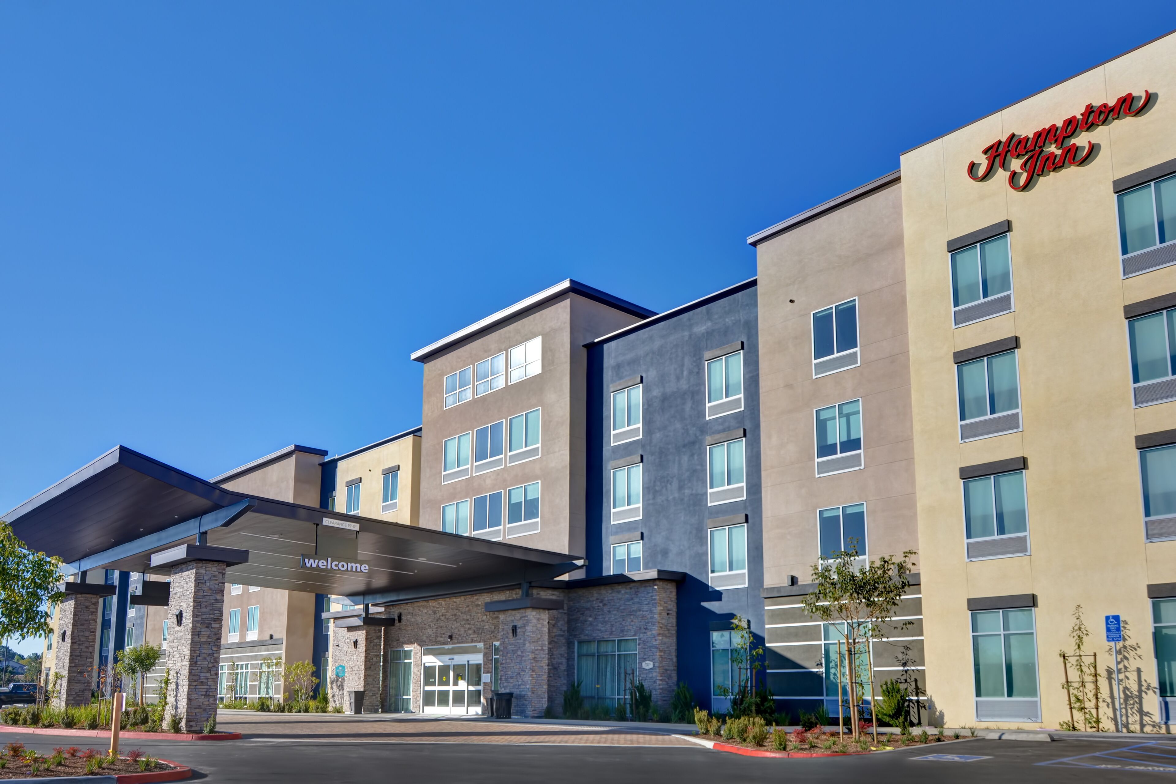 A modern hotel with a 'Welcome' sign, multiple floors, and a covered entrance.