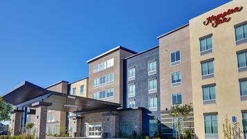 A modern hotel with a 'Welcome' sign, multiple floors, and a covered entrance.