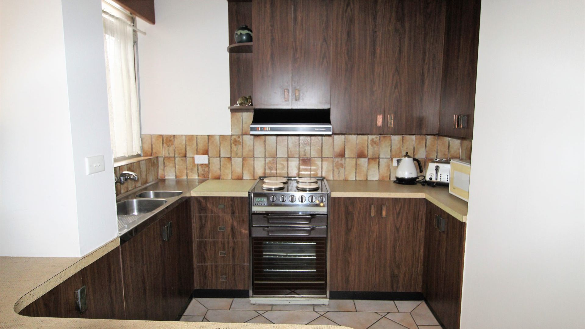 A kitchen with dark wooden cabinets, a gas stove, a microwave, and a kettle.