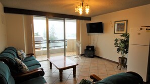Un salon comprenant un ensemble de canapés, une table basse, un téléviseur fixé au mur et un balcon avec vue.