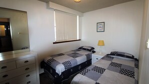 A bedroom with two beds, a dresser, a window with blinds, a lamp, and a framed picture on the wall. - Macquarie Towers 17, 1 Waugh Street (Port Macquarie)