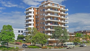 A multi-story residential building with balconies, surrounded by greenery and parked vehicles.