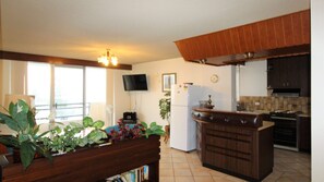 A kitchen with a central island, a built-in oven, and a dining area with a bench and potted plants.