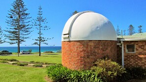 A building with a dome structure, surrounded by a grassy area, trees, and a view of the ocean. - Ocean Court 8, 13 Lord Street (Port Macquarie)