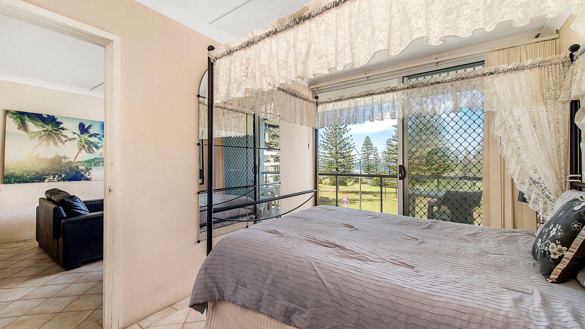 A bedroom with a bed, a chair, a window with curtains, and a view of trees and a building.