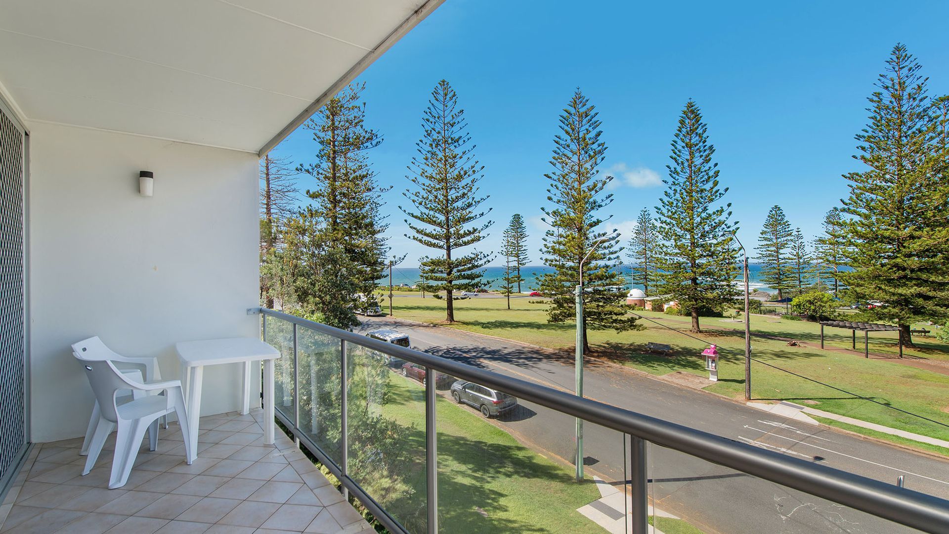 A balcony with a view of a road, trees, and a body of water.
