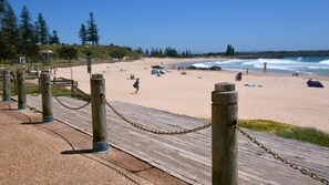 A wooden boardwalk leading to a sandy beach with a clear sky. - Ocean Court 8, 13 Lord Street (Port Macquarie)