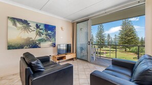 A balcony with a TV, leather sofas, and a painting of a beach scene. - Ocean Court 8, 13 Lord Street (Port Macquarie)