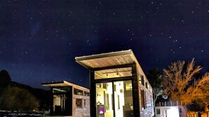 A modern, two-story building with a glass facade, illuminated interior, and a starry night sky. - Cliffside Cabin   # 2 (St Orderville)