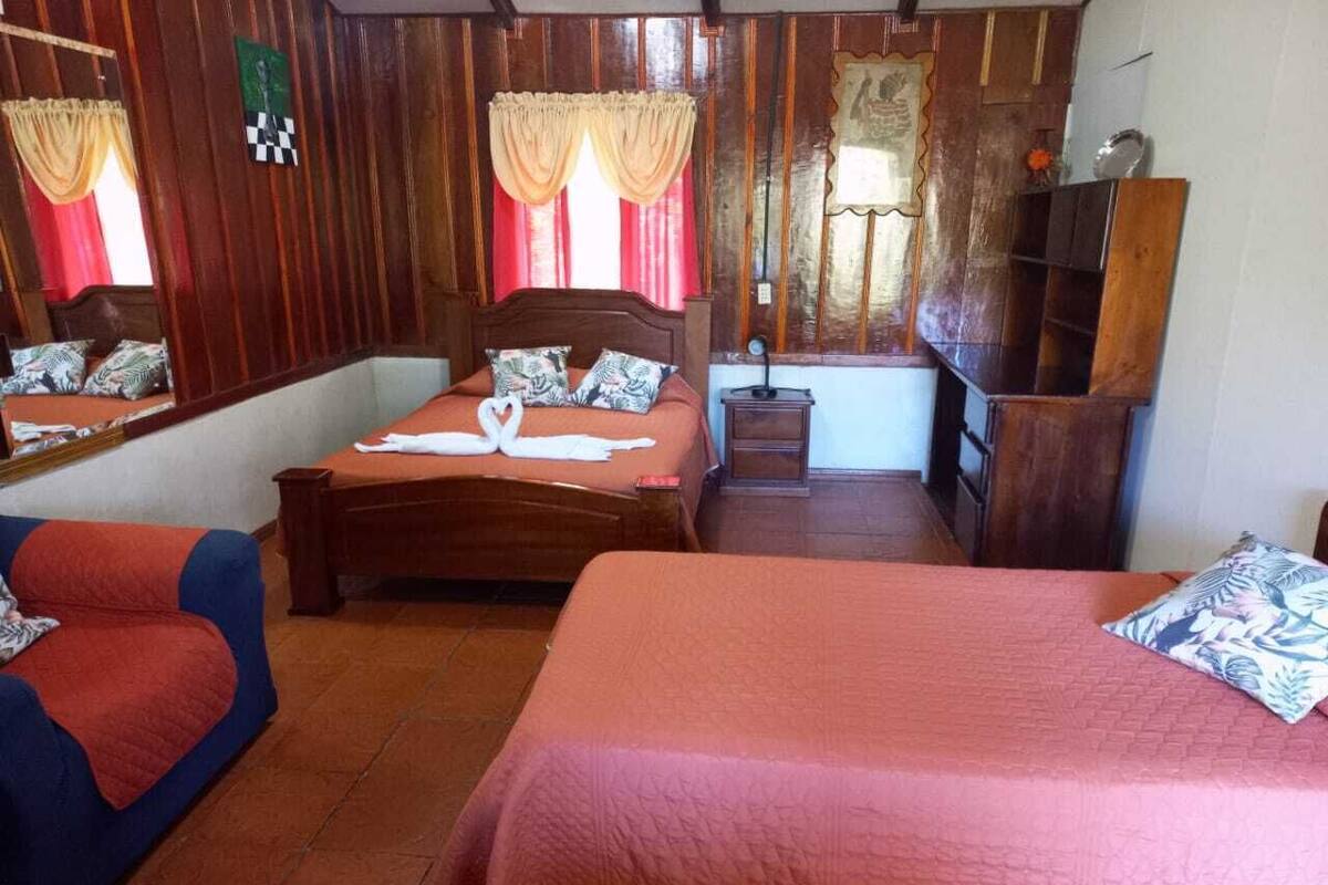 A room with two beds, a sofa, a wooden wardrobe, and a mirror.
