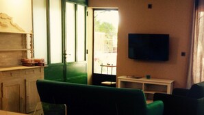 Ein Wohnzimmer mit grünem Sofa, einem Wand-Fernseher und einem Esstisch.
