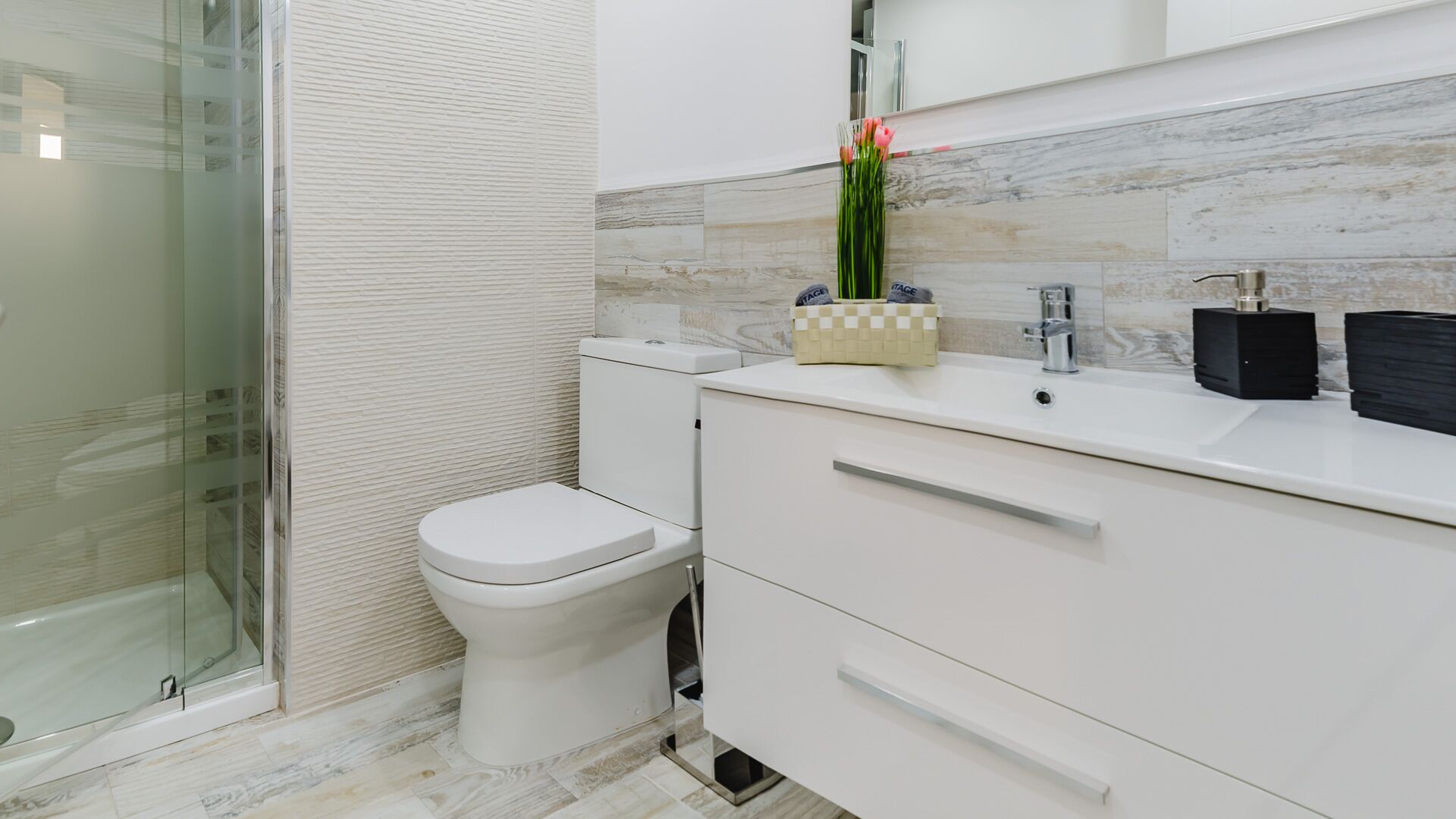 Ein modernes Badezimmer mit Toilette, Duschkabine aus Glas sowie Waschtisch mit Becken und Spiegel.