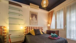 A hotel room with a bed, a chair, a glass shelf, a painting, and a window with curtains. - Historic apartment house with exceptional situation and kept facility (Granada)