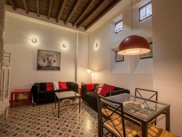 Una sala de estar acogedora con un sofá, una mesa de vidrio y una lámpara roja.