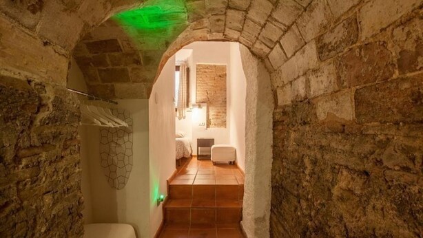 A narrow stone corridor with a tiled floor leading to a room with a bed and a window. - Historic apartment house with exceptional situation and kept facility (Granada)