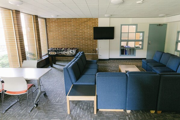 A room with blue seating, a foosball table, a TV, and a window with a view.