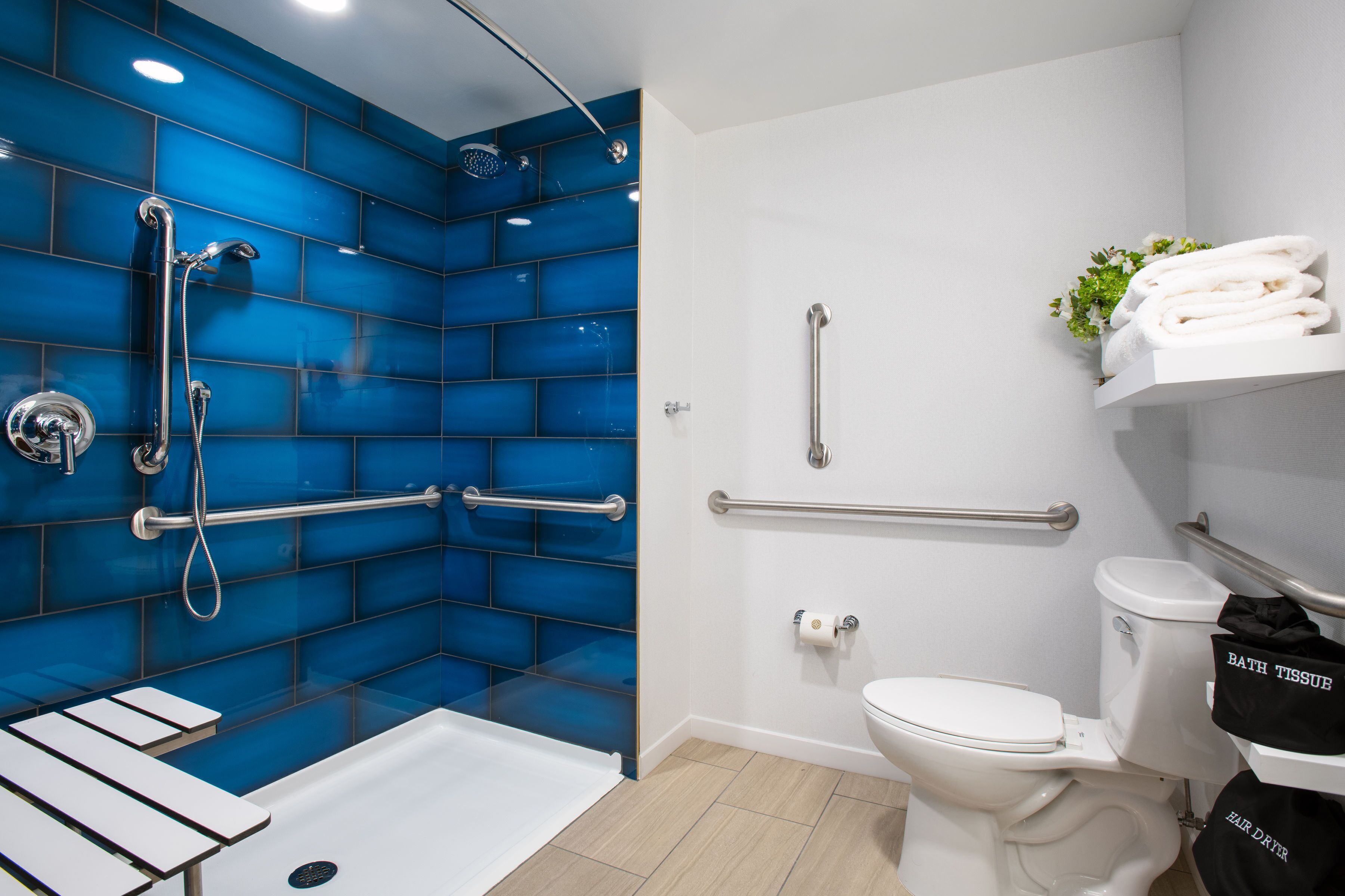 A bathroom with a blue-tiled shower area, a white toilet, and a white sink.