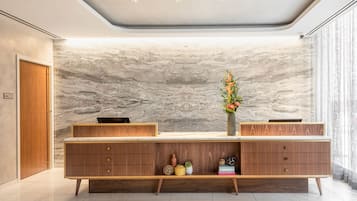 Una moderna recepción con un fondo de pared de mármol, cajones de madera y un florero con flores.