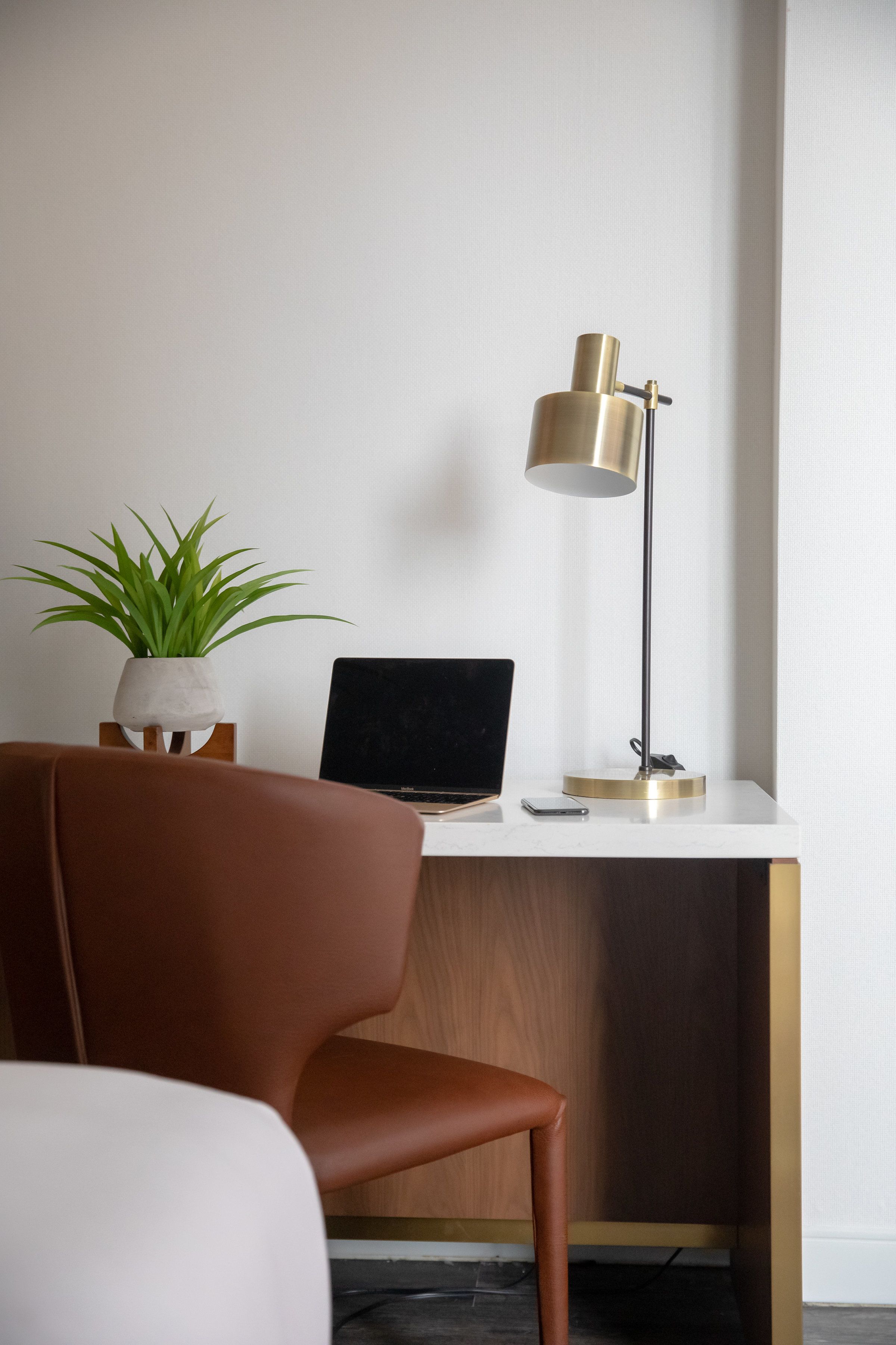 A workspace with a laptop, a desk lamp, a potted plant, and a brown chair.