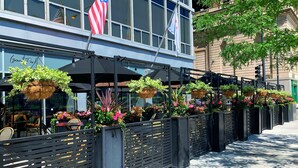 Un restaurante con terraza al aire libre, cubierto por sombrillas y decorado con macetas colgantes.