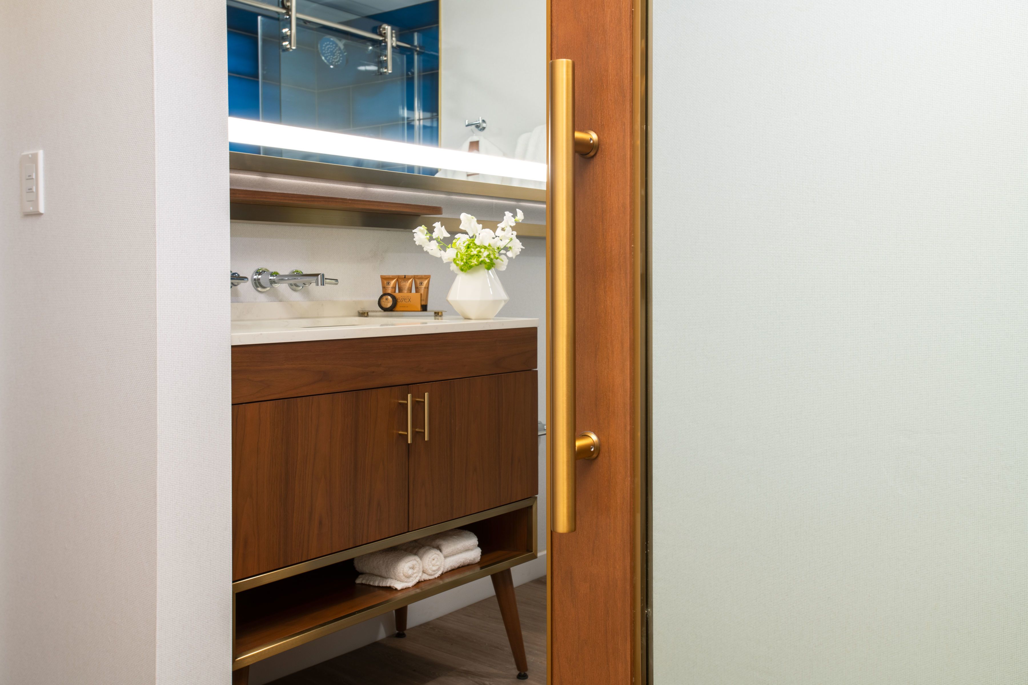 A bathroom with a wooden vanity, a white sink, a mirror, and a vase with flowers.