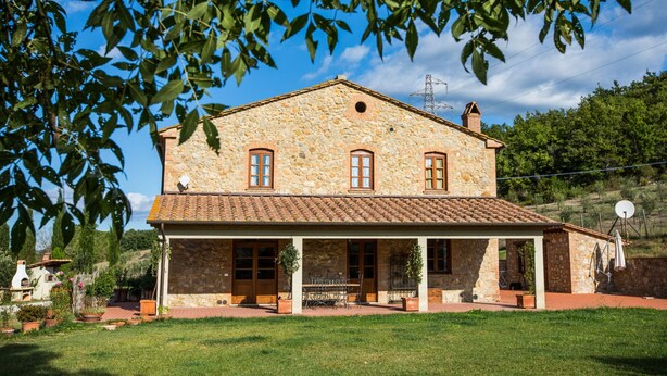 Una casa de pedra amb teulada de rajola, un porxo cobert i un jardí.