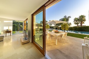Una sala de estar moderna con un gran ventanal corredero que da a un patio exterior con piscina y palmeras.