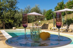 A poolside setting with a table featuring glassware and a fruit bowl.