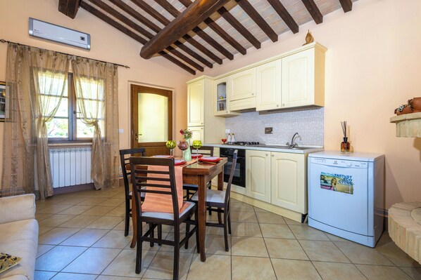 A kitchen with wooden cabinets, a dining table with chairs, a refrigerator, and a window with curtains.