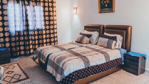 A bedroom with a bed, a nightstand, a lamp, a painting, and a patterned curtain. - Casa Karam With View Of The 3 Mountains (chefchaouen)