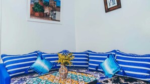 A room with a blue-striped sofa, a small table with a vase, and two framed pictures on the wall. - Casa Karam With View Of The 3 Mountains (chefchaouen)