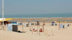 Ein Strand mit Zelten, Liegestühlen und einer Flagge.