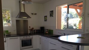 Eine moderne Küche mit weißen Schränken, Edelstahlgeräten, einer schwarzen Arbeitsplatte und einem Fenster mit Blick auf Grünflächen.