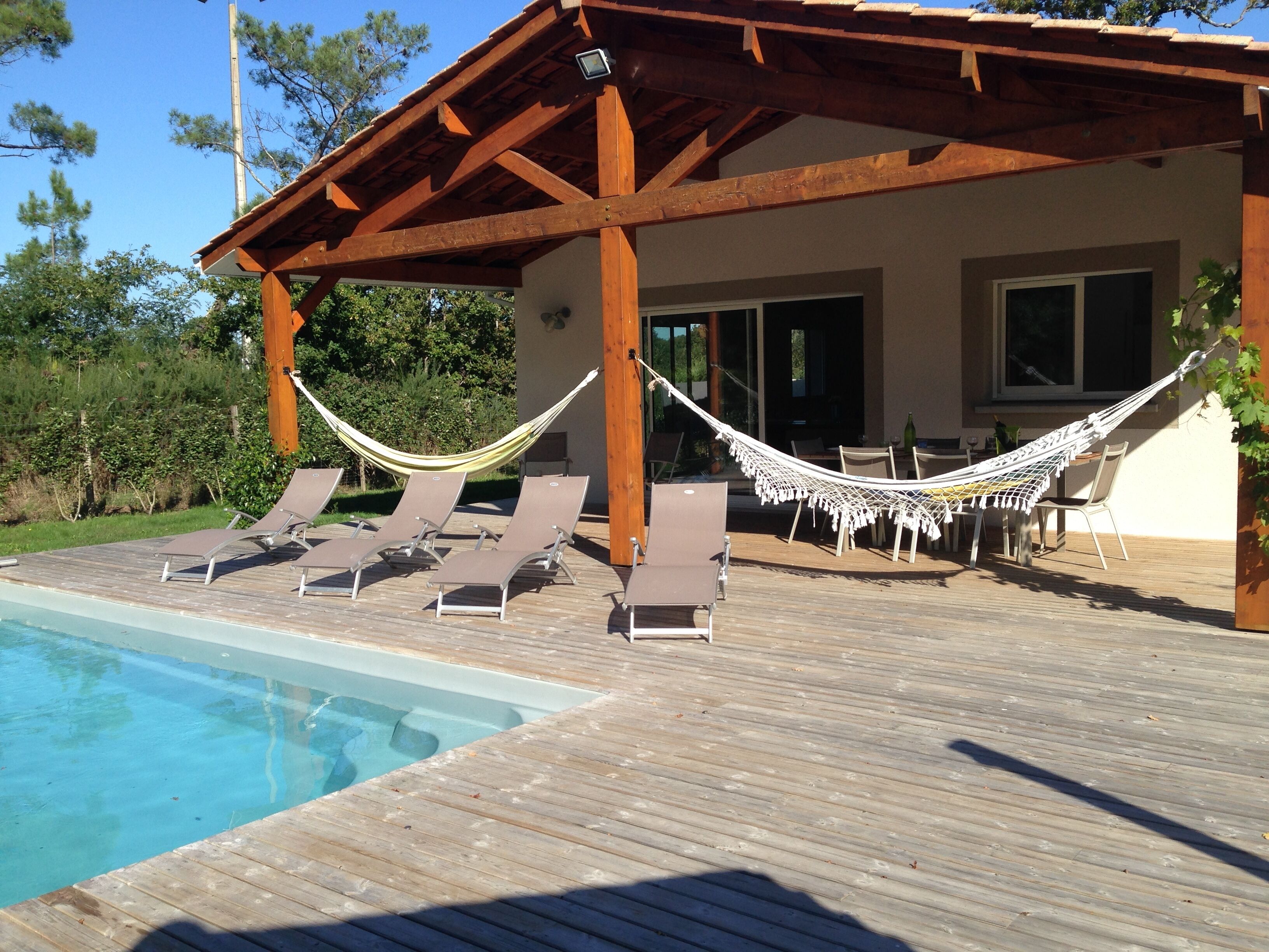 A wooden deck with a pool, lounge chairs, and a hammock.
