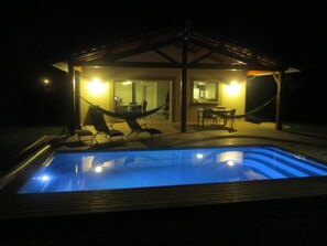 A pool with lounge chairs and a covered seating area at night. - Holiday home with heated swimming pool (Grayan-Et-L'hôpital)