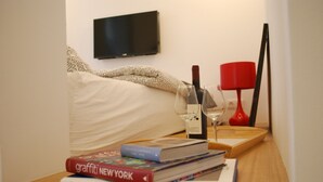 A neatly arranged hotel room with a bed, a bedside table with books and a wine glass, a TV mounted on the wall, and a red lamp. - Art Aldebaran: a magical feeling in the City Center with A/C! (VI. kerület)