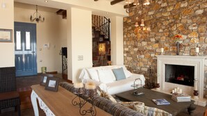 A cozy living room with a stone wall, a fireplace, a white sofa, and a wooden coffee table. - luxury villa,Mesinnia,penthouse sea view, family,reunions,swimming pool,leisure  (Messini)