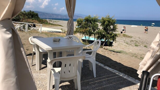 Une vue sur la plage depuis un espace abrité, équipé d’une table et de chaises, d’où l’on peut admirer la mer et la plage.