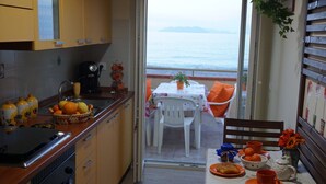 Une cuisine avec vue sur la mer, une table à manger avec des coussins orange et une petite table avec une théière et des tasses orange.